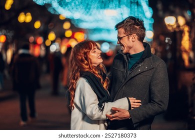 Portrait of a young affectionate couple standing on city street at night and hugging on christmas or new year's eve. A romantic and festive couple is celebrating christmas or new year on city street. - Powered by Shutterstock