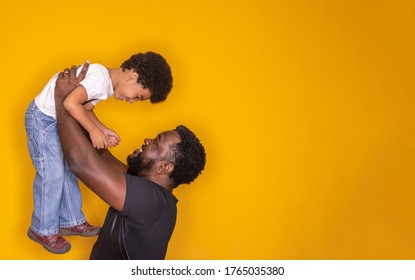 Portrait Of Young African American Father With Toddler Son. Yellow Background. Brazilian Family. Fathers Day Concept! 
