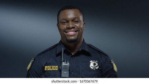 Portrait of the young African American good looking and cheerful policeman smiling to the camera. Close up.