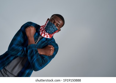 Portrait Of Young African American Man Wearing Bandana Mask Showing Cross Gesture Protesting For Human Rights, Looking At Camera While Posing Isolated Over Gray Background. Social Issues. Dutch Angle