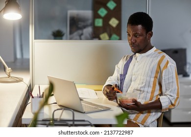 Portrait Of Young African American Man Eating Healthy Snack While Working Or Studying Late At Night