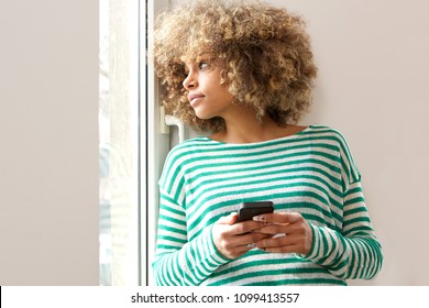 Portrait of young african american woman holding mobile phone and looking out window