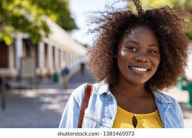 Portrait of young african american woman with curly hair smiling and looking at camera. Black curvy girl in casual clothes enjoying outdoor. Pretty black college student in campus.