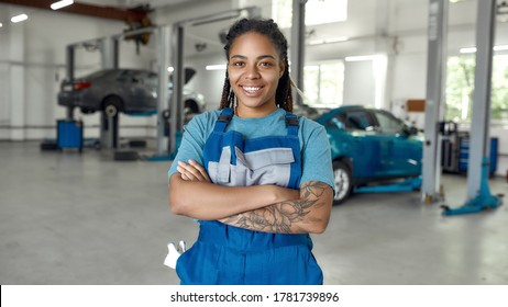 Portrait Of Young African American Woman, Professional Female Mechanic Smiling At Camera Standing In Auto Repair Shop. Car Service, Repair, Maintenance And People Concept. Front View. Web Banner