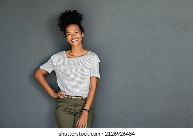 Portrait von jungen Afro-Amerikanern, die mit Händen auf der Taille stehen und die Kamera anschauen. Zuversichtliche, stylische, schwarze Frau, die auf grauem Hintergrund steht. Fröhlich nach Mädchen lächeln mit Kopienraum.