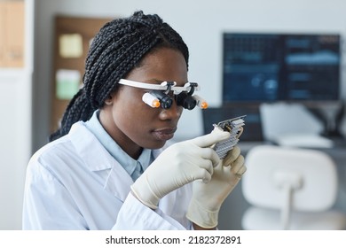 Portrait of young African American woman wearing magnifying visor and inspecting hardware part in engineering laboratory - Powered by Shutterstock