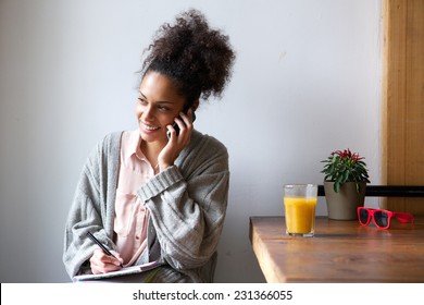 Portrait Of A Young African American Woman Talking On Mobile Phone And Taking Notes