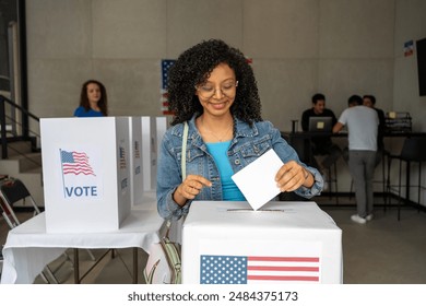 portrait of a young african american woman voting in the us election, placing vote ballot in the polling box, vote in America. Concept of choice, democracy and freedom - Powered by Shutterstock