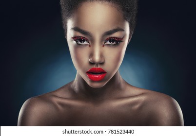 Portrait of a young African American woman with a glamorous make-up and red lips on a dark background. Fashion makeup. 