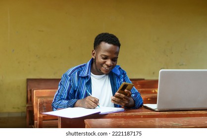 Portrait of a young african boy using a digital phone while doing his homework - Shutterstock ID 2221187175