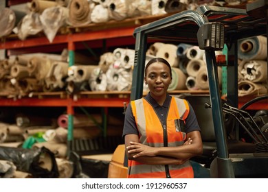 Portrait of a young African female forklift operator standing with her arms crossed in a textile warehouse - Powered by Shutterstock