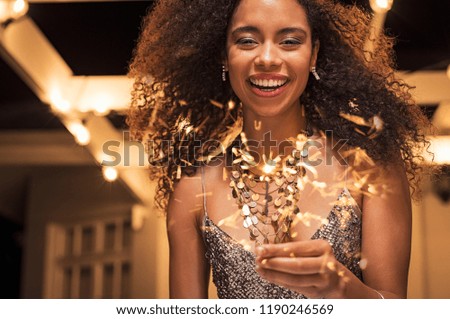 Portrait of young african girl holding sparkle stick under the patio outdoor. Happy smiling woman celebrating with fireworks. Elegant woman holding a bengal light for new year’s eve party.