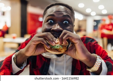 A Portrait Of Young African Man Eating A Burger In Street Food Cafe. Fast Food Eating Time.