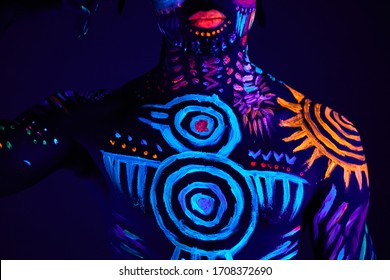 portrait of young african man in UV paint isolated. bright fluorescent body art glows in darkness, ethnic prints on naked skin and face