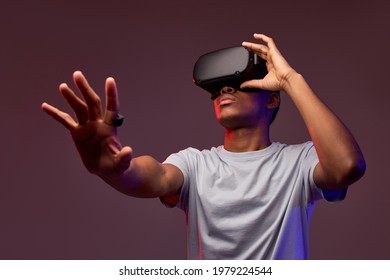 Portrait of young african teen boy in VR helmet looks away at copy space, isolated in studio, guy holds out hand forward. Gamer playing VR games on colourful background, VR gaming. - Powered by Shutterstock