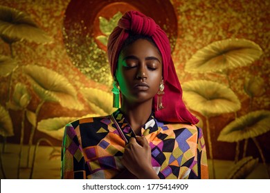 Portrait Of A Young African Woman With Closed Eyes In Ethnic Clothes. Red Scarf On The Head, Gold Earrings. Blurred Background With Gold Ornaments. Fashion