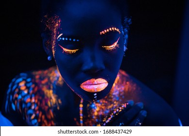 portrait of young african woman with colorful abstract make-up on face. unusual, interesting, fantastic shoot. body art, neon lights, fluorescence