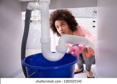 Portrait Of An Young African Woman Looking At Water Leaking From Sink Pipe