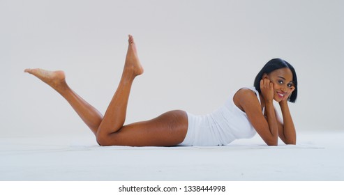 Portrait of young african  woman with perfect body lying on the floor and showing her hairless soft and silky legs after depilation isolated on a white background.