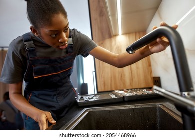 Portrait Of Young African Woman, Professional Plumber In Overalls, Installing Black Contemporary Kitchen Faucet. Gender Equality Concept.