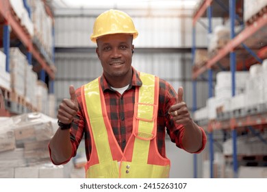 Portrait of young African worker man wearing safety vest and helmet standing and giving thumbs up at warehouse factory. Male cargo logistics staff working at shipping storehouse workplace. - Powered by Shutterstock