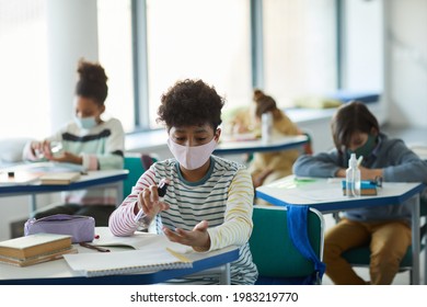 Portrait Of Young African-American Boy Sanitizing Hands In School Classroom, Covid Safety Measures, Copy Space