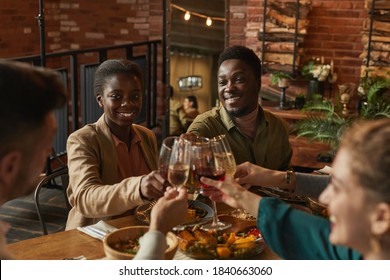 Portrait Of Young African-American Couple Clinking Glasses While Enjoying Dinner Party With Friends And Family In Cozy Interior