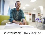 Portrait of young African-American man reading braille while studying in school library, copy space