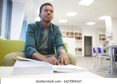 Portrait of young African-American man reading braille while studying in school library, copy space
