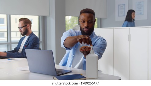 Portrait of young african-american man sanitizing hands while working in office. Black office employee working on laptop and cleaning hands with antiseptic gel - Powered by Shutterstock