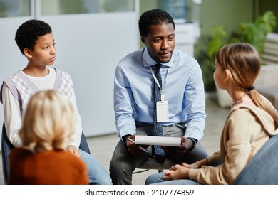 Portrait of young African-American psychologist listening to children in support group circle