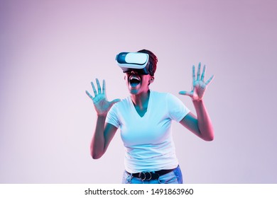 Portrait of young african-american woman's playing in VR-glasses in neon light on gradient background. Concept of human emotions, facial expression, modern gadgets and technologies. Touches something. - Shutterstock ID 1491863960