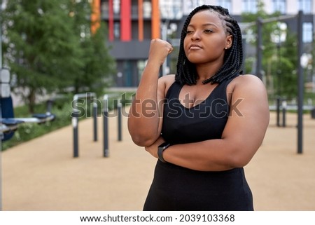 Portrait of young afro american woman in black tracksuit posing at camera, have rest, black fat lady is looking serious and confident, copy space. Sport, healthy lifestyle, workout, fitness concept