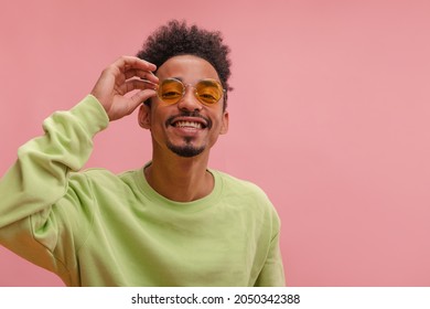 Portrait of young afro man, touching his classy eyewear, looking at camera with joy. Medium shot of beauty brown-skinned man with curly hair, dressed up casual against pink wall. - Shutterstock ID 2050342388