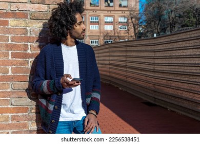 Portrait of young afro man using his mobile phone against brick wall. Technology and lifestyle concept.