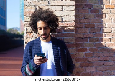 Portrait of young afro man using his mobile phone against brick wall. Technology and lifestyle concept.
