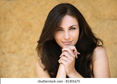 Portrait of young alluring smiling attractive brunnete woman propping up her face against yellow background.