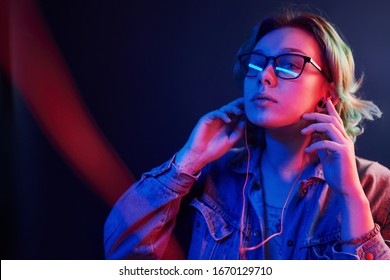 Portrait Of Young Alternative Girl In Glasses With Green Hair In Red And Blue Neon Light In Studio That Listening To Music In Headphones.