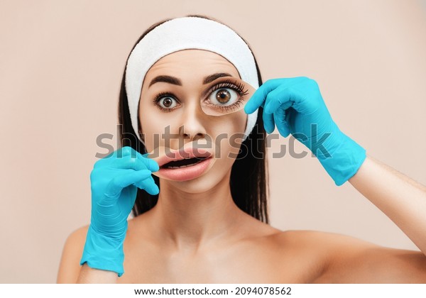 Portrait of a young amazed woman\
holding magazine clippings of eyes and lips on her face. Beige\
background. The concept of plastic surgery and aesthetic\
medicine.