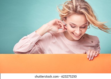 Portrait of young amazing blonde woman in light pink dress looking down in studio with turquoise background and orange sheet