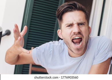 Portrait of a young angry man gesticulating with his hands, looking ant the camera. A millennium man screaming, indoors, terrace