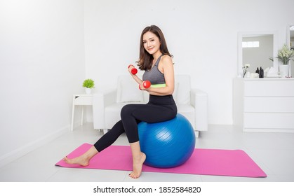 Portrait Of Young Asian Attractive Fitness Woman Holding Dumbbell Sitting On Big Ball At Home. Sport Ware Girl Workout With Strong Beautiful Fit Body Shape, Asia Lifestyle With Copy Space