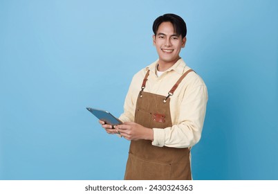 Portrait young asian barista man wearing apron holding tablet standing and smile isolated on blue background, waitress or entrepreneur cheerful, small business or startup, - Powered by Shutterstock