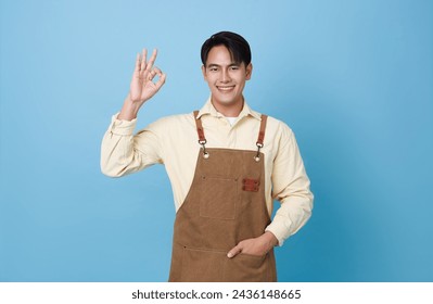 Portrait young asian barista man wearing apron standing gesturing OK sign isolated on blue background, waitress or entrepreneur cheerful. - Powered by Shutterstock