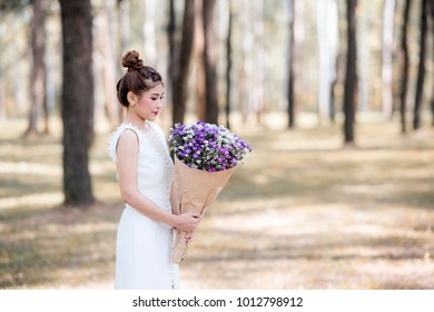 Portrait of young asian bride in white lace wedding dress holding bouquet of purple flower