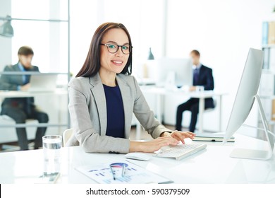 Portrait of young asian business analyst typing at modern computer sitting at her workplace in light office with statistics document beside her - Powered by Shutterstock