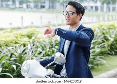 Portrait Of Young Asian Businessman Riding On Scooter And Checking Time Or Notifications On His Smartwatch