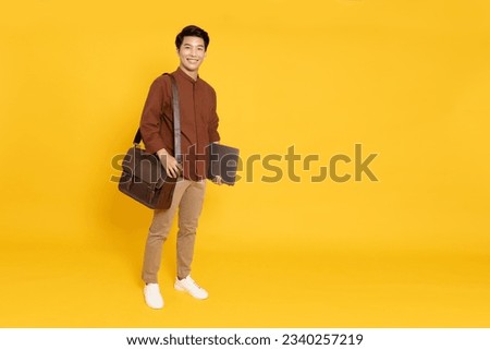 Portrait of young Asian businessman smile and holding laptop and brown leather bag isolated on yellow background, Full body composition
