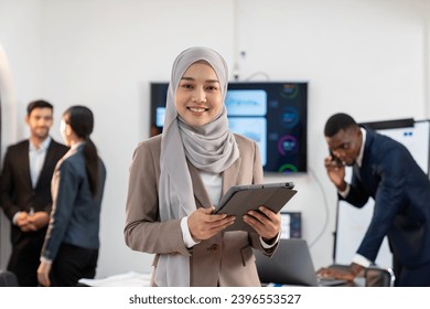 portrait of young asian businesswoman in formal suit with tablet standing in the international office,  group of multiracial team colleague diverse employee coworker meeting for financial performance - Powered by Shutterstock