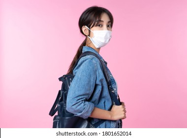 Portrait of young Asian college student wears face mask and backpack isolated over pink background - Powered by Shutterstock